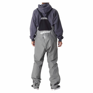 A man wearing a pair of grey fishing bibs from behind, with a white hewes logo on the lower back.