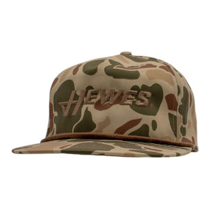 A brown camouflage snapback hat with the hewes logo across the front. 